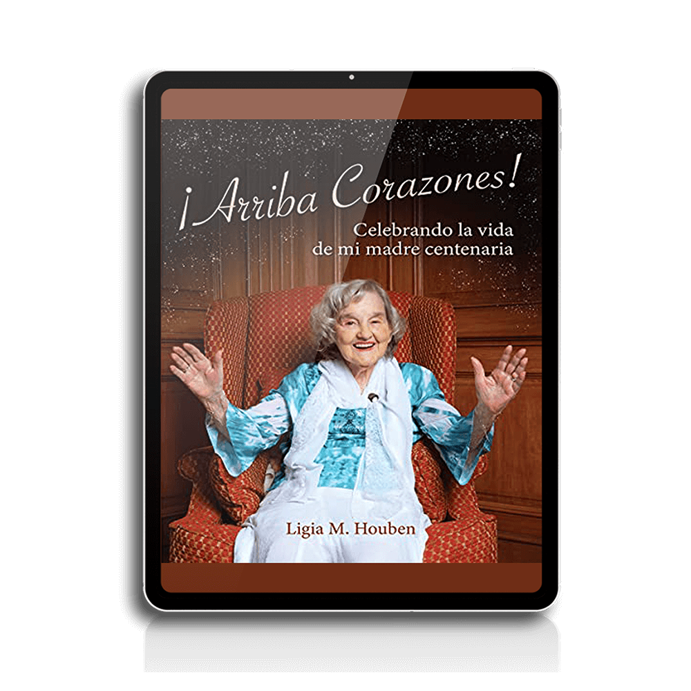 Ebook cover of "¡Arriba corazones! Celebrando la vida de mi madre centenaria" by Ligia M. Houben, featuring a smiling elderly woman in a blue outfit, sitting on a patterned chair, with hands raised in celebration.